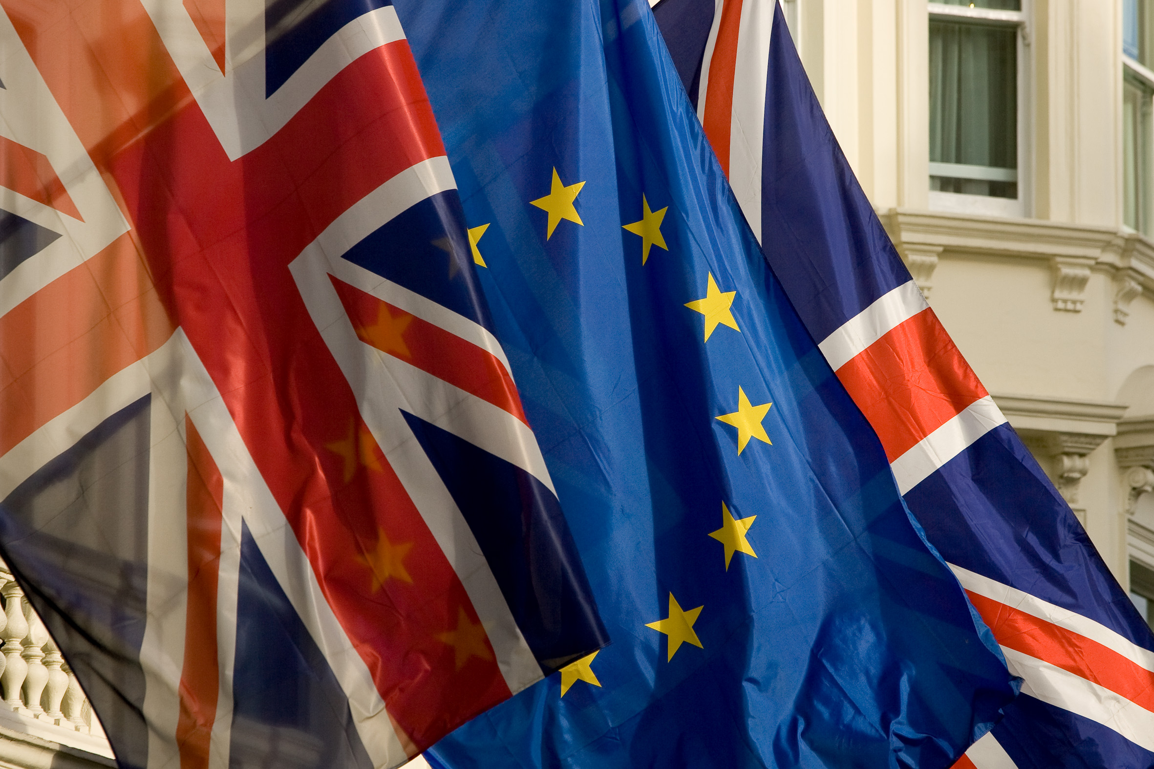 Flagi Wielkiej Brytanii i Unii Europejskiej powiewają przedz zabytkowym budynkiem.